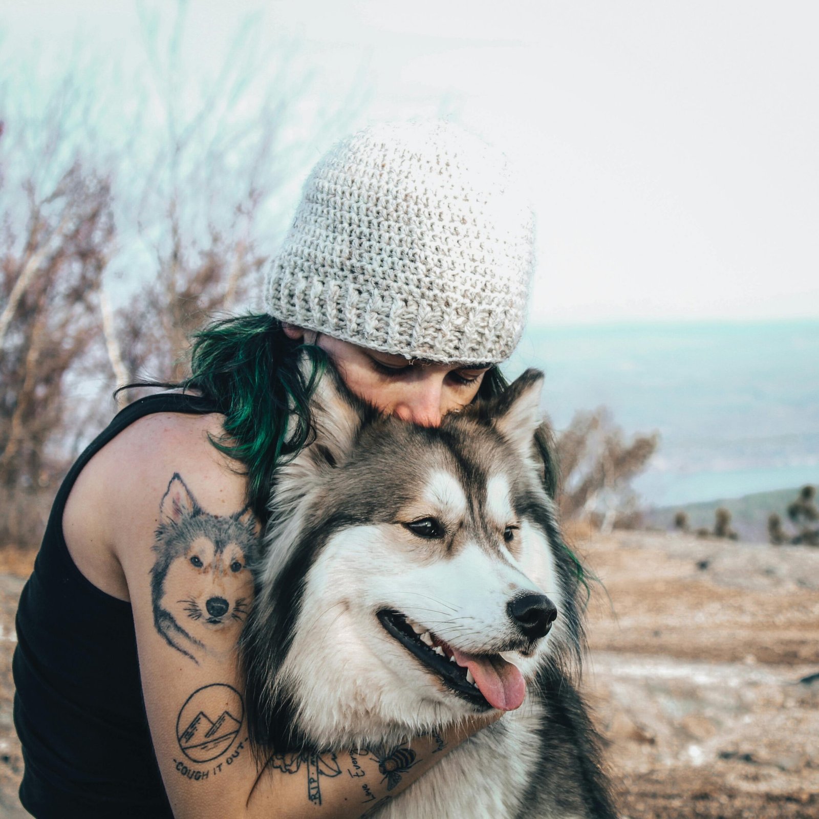 Chica con tatuajes abrazando a perro de raza alaskan malamute